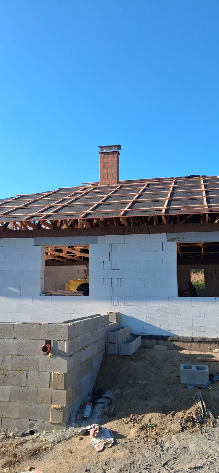 Dokončený zděný komín nad střechou novostavby zakončený nerezovou krycí deskou